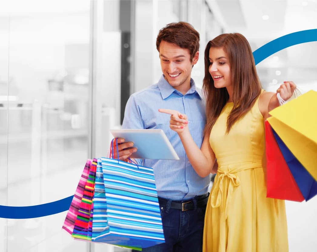 a happy couple shopping, holding bags and looking at a tablet